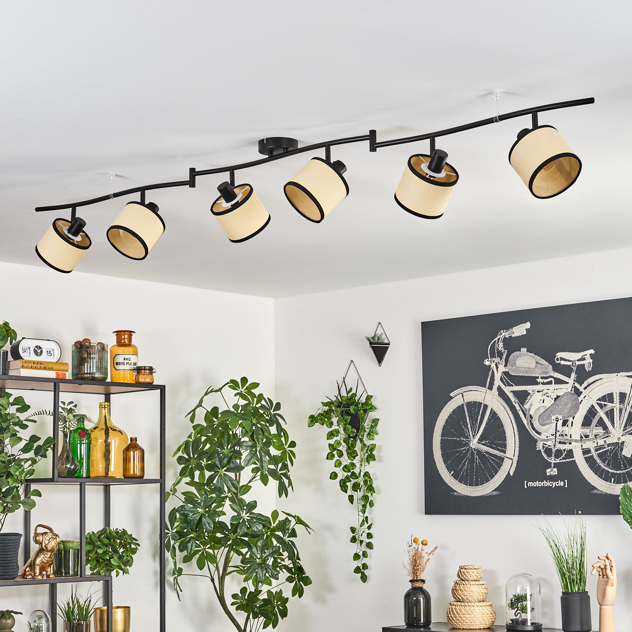 Eine moderne Deckenleuchte mit sechs Lampen. Es gibt Pflanzen, ein Gemälde eines Motorrads und andere Dekorationsgegenstände im Raum.