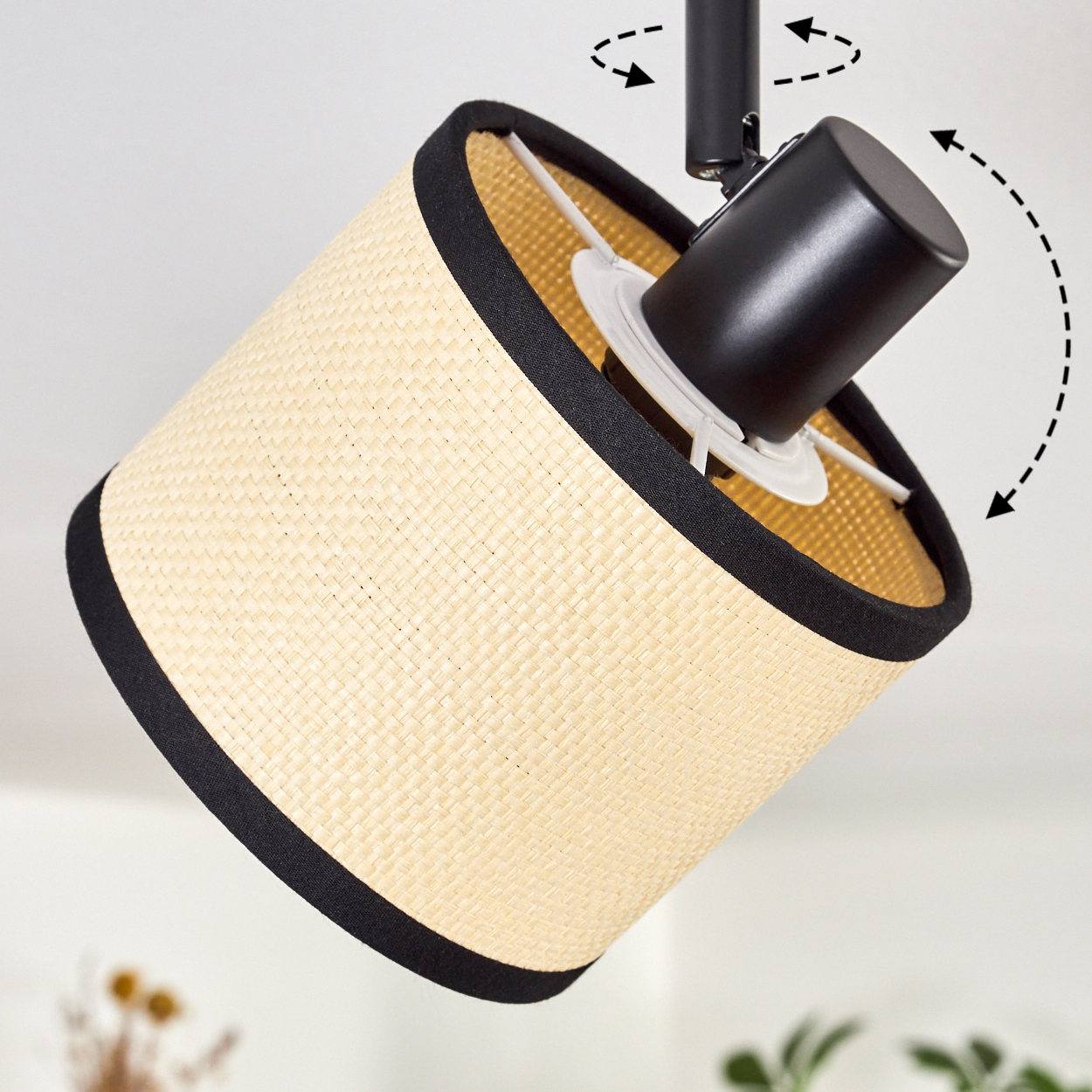 Eine Lampe mit gewebtem Schirm und schwarzem Rand. Die Lampe ist schwarz und abgewinkelt. Pfeile zeigen die Verstellbarkeit.