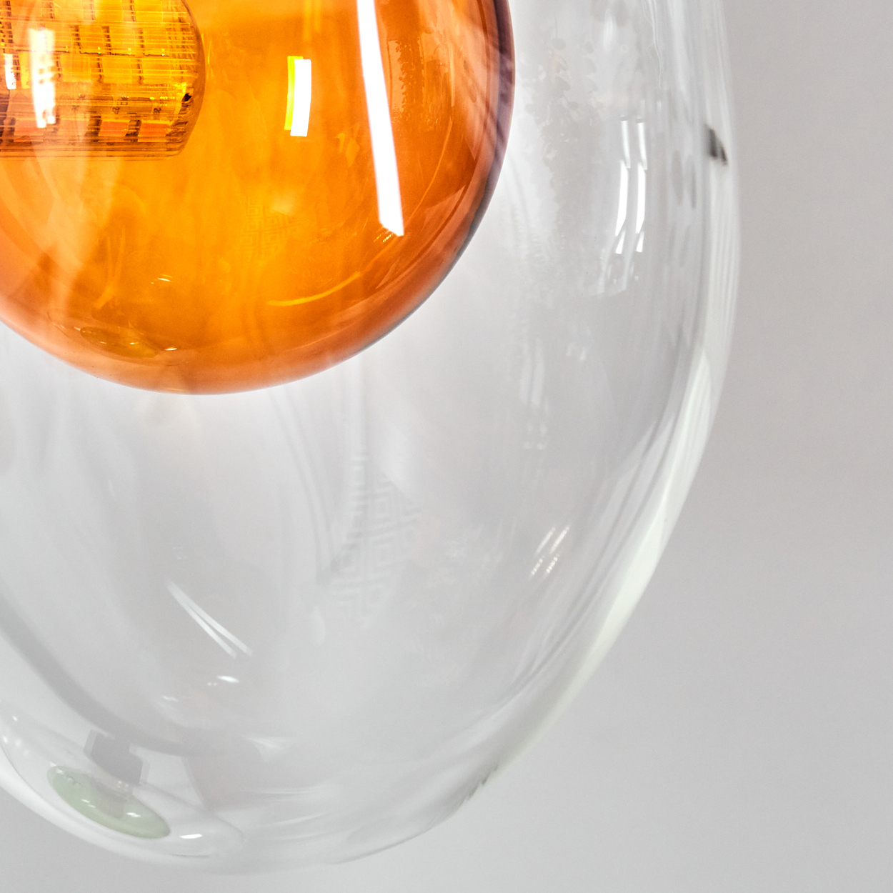 Nahaufnahme eines durchsichtigen Glasobjekts mit einer orangefarbenen, beleuchteten Kugel im Inneren, vor weißem Hintergrund.