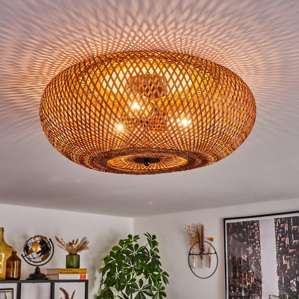 Eine Deckenlampe aus gewebtem Bambus wirft ein gemustertes Licht. Darunter steht ein Regal mit Dekoration und einer grünen Pflanze.