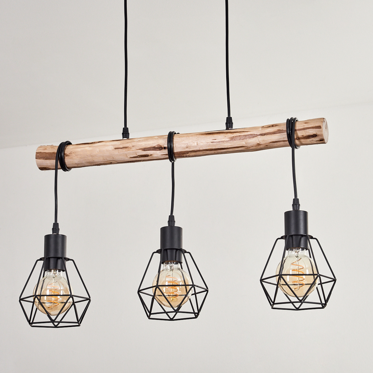 Ein Holzbalken mit drei schwarzen Pendelleuchten. Jede Leuchte hat einen käfigartigen Schirm mit einer sichtbaren Glühbirne.
