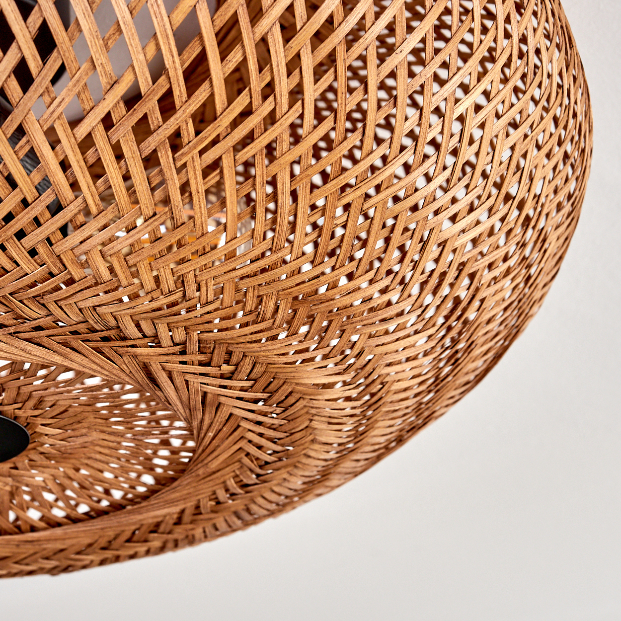 Nahaufnahme eines gewebten Lampenschirms aus Rattan. Der Schirm ist braun mit einem komplexen Muster vor weißem Hintergrund.