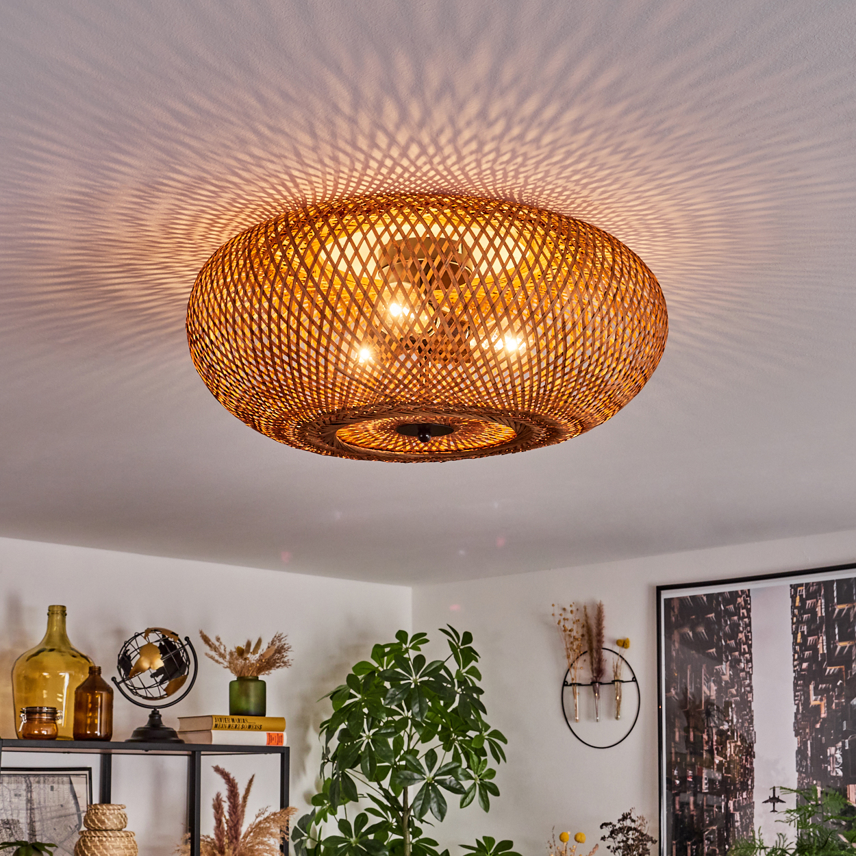 Eine Deckenlampe aus Korb wirft Lichtmuster an die Decke. Darunter eine Zimmerecke mit Deko, Pflanze und gerahmtem Bild.