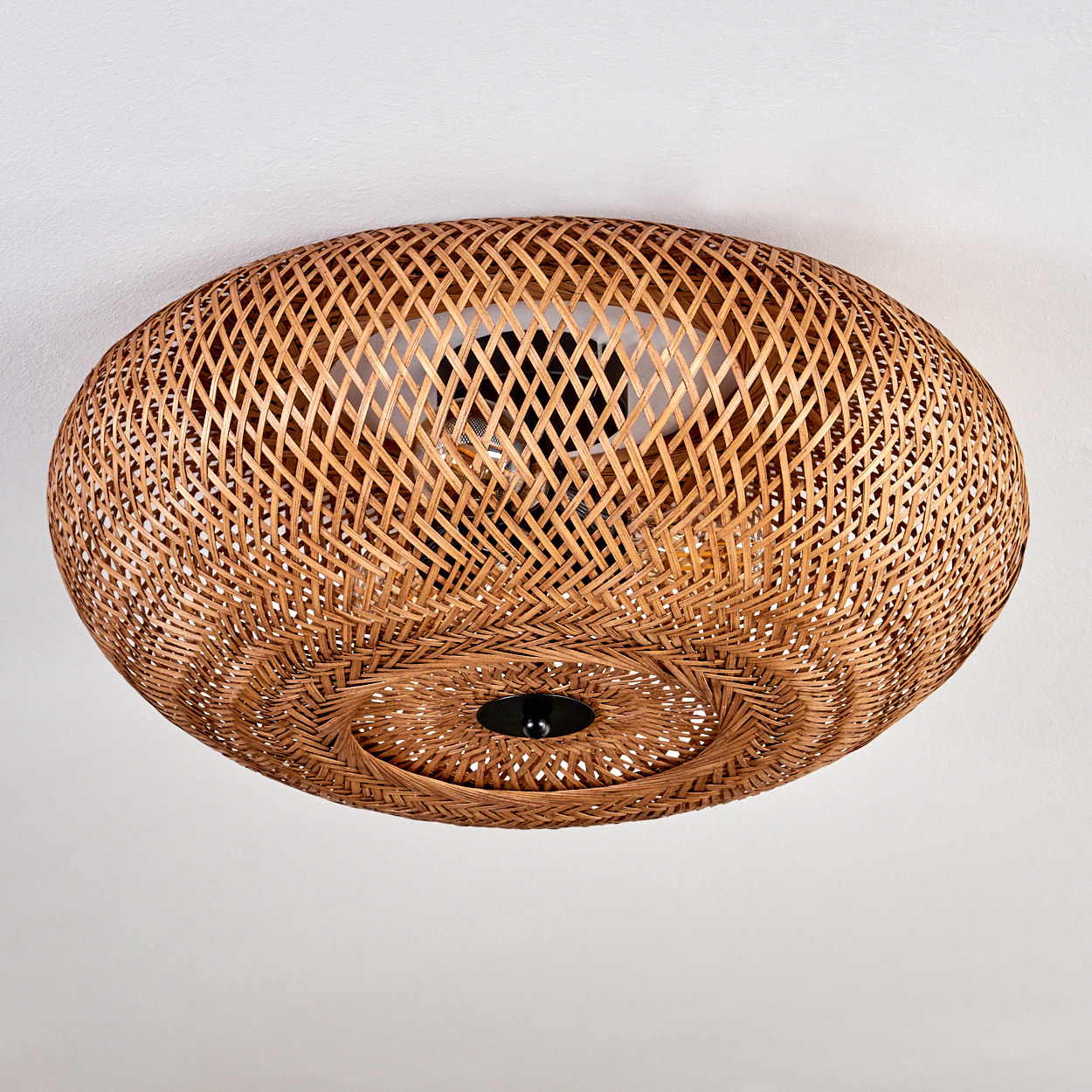Eine gewebte Deckenlampe aus Rattan, braun, mit schwarzem Mittelteil und weißem Deckenhintergrund. Die Lampe ist kreisförmig.