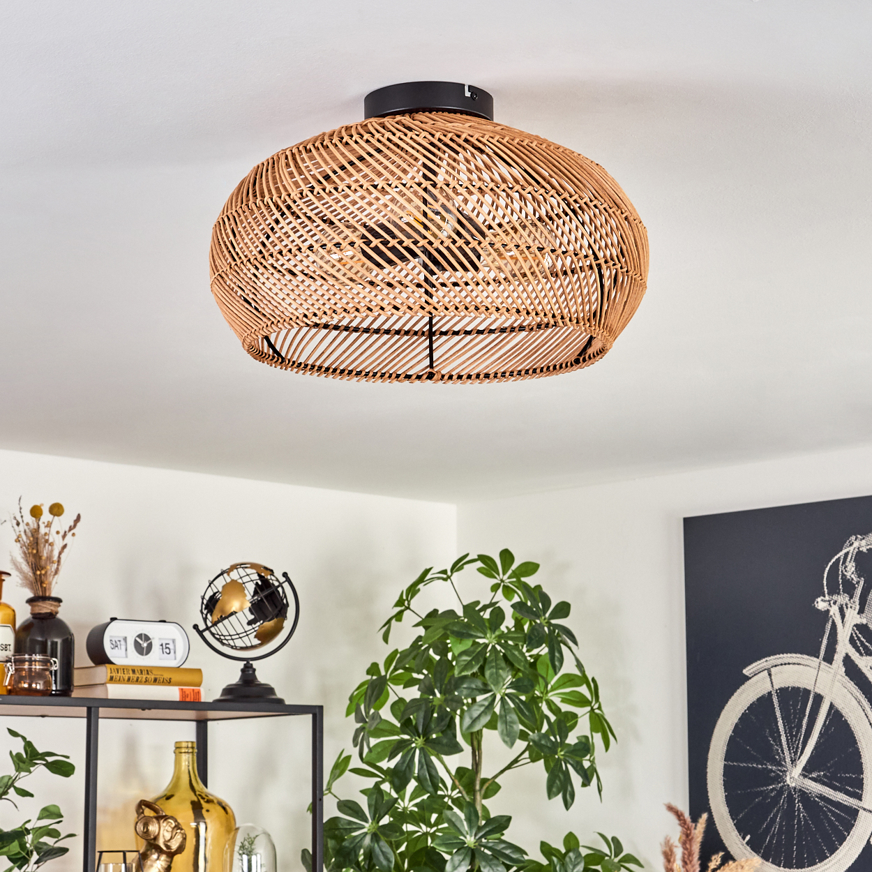Eine Deckenleuchte aus geflochtenem Rattan. Darunter ein schwarzes Regal mit Deko, einem Globus und Pflanzen. Rechts ein Fahrradkunstwerk.