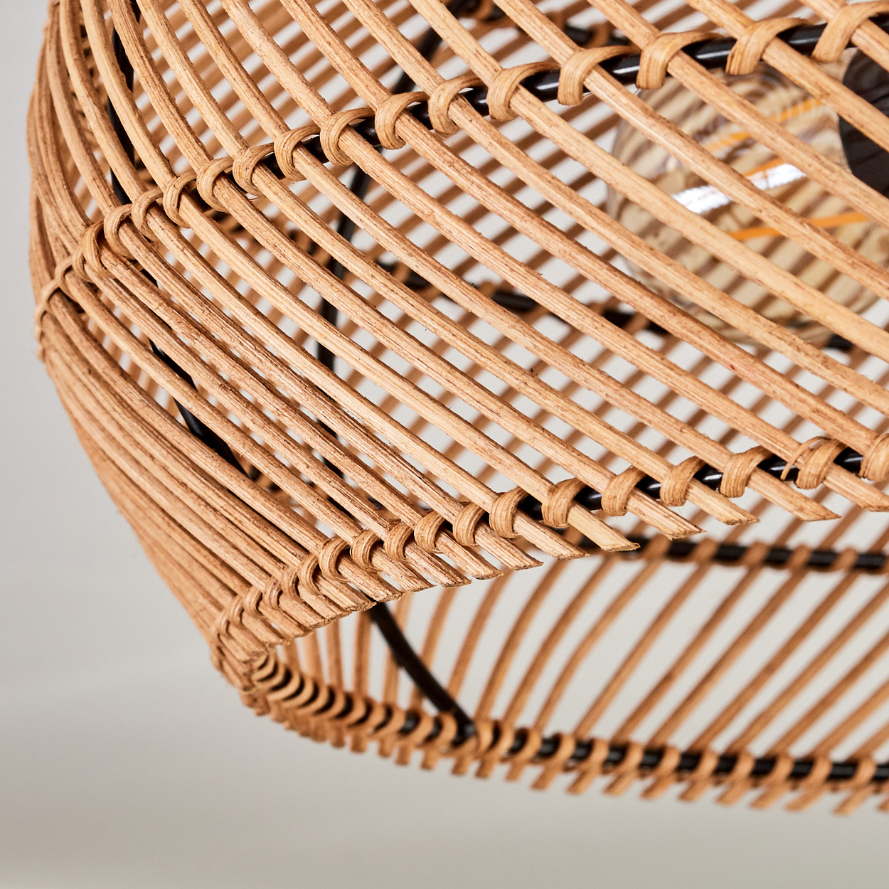 Nahaufnahme eines Lampenschirms aus geflochtenem Rattan. Der hellbraune Schirm hat ein korbartiges Geflecht mit sichtbarer schwarzer Metallstütze.
