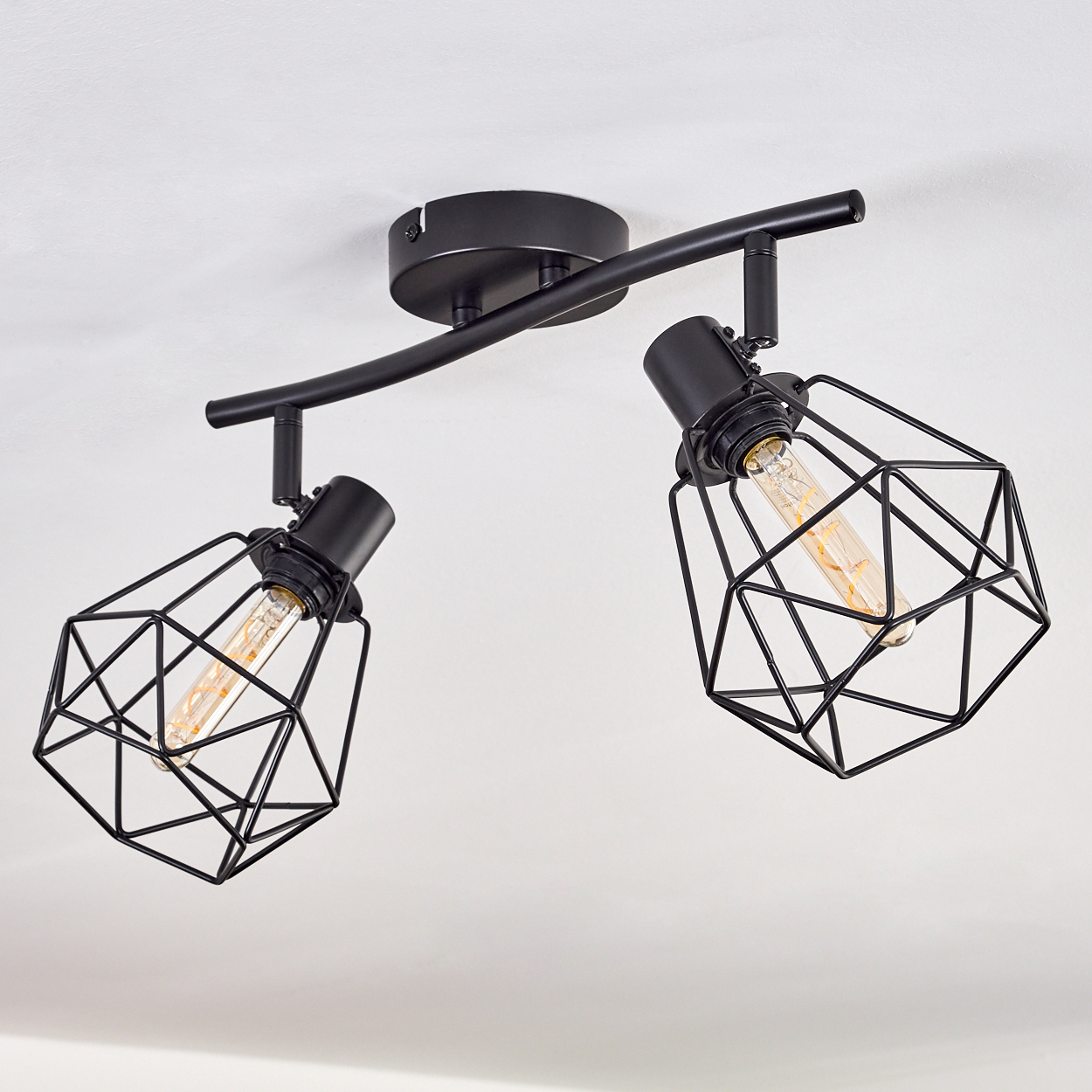 Schwarze Deckenleuchte mit zwei Lampen. Jede Lampe hat einen geometrischen Käfig und eine sichtbare Glühbirne. An der Decke montiert.