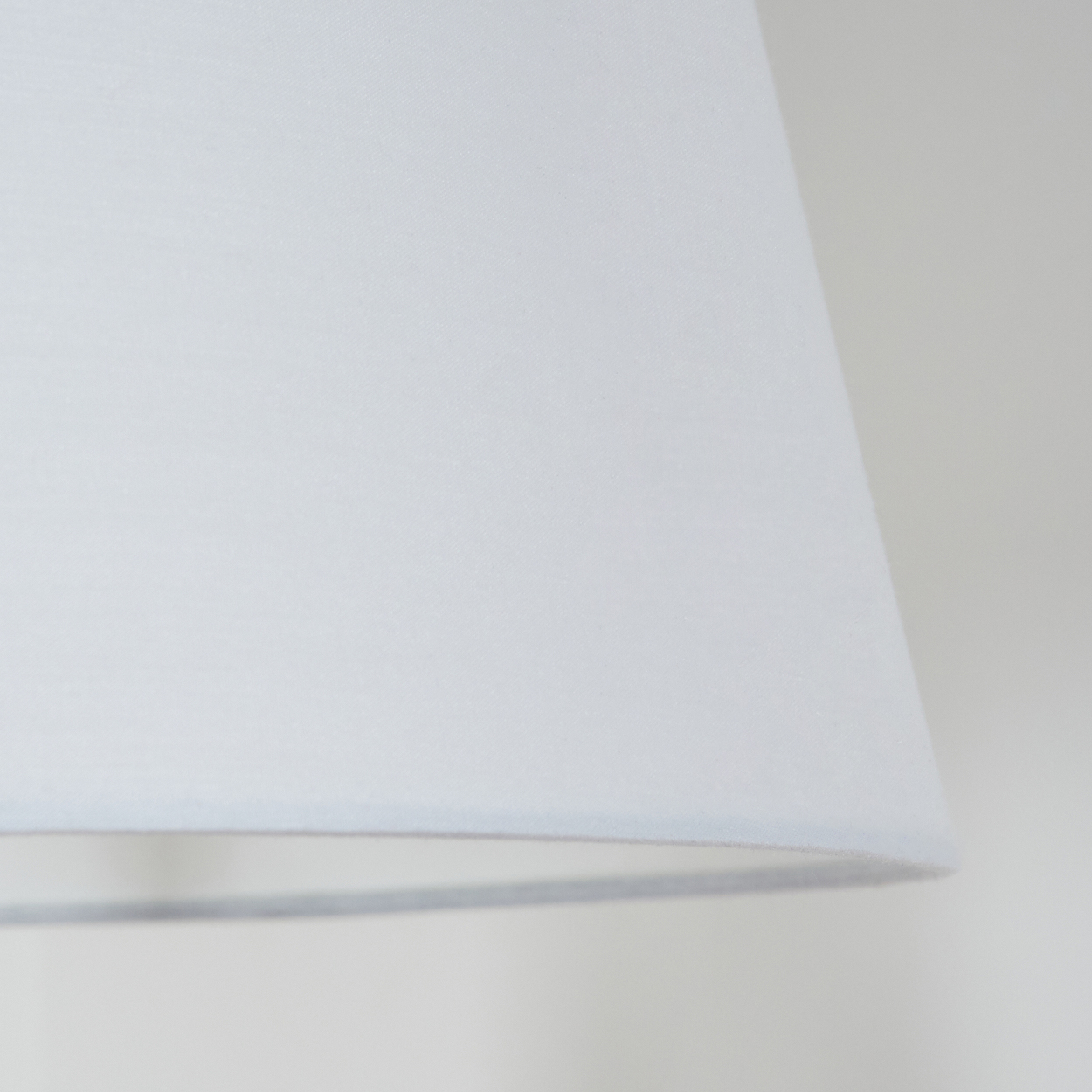Nahaufnahme eines weißen Lampenschirms. Der Schirm hat eine Trapezform. Der Hintergrund ist eine schlichte, cremeweiße Wand.