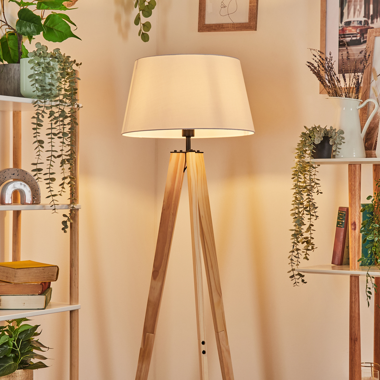 Eine Holzstativlampe beleuchtet eine Ecke mit Regalen voller Pflanzen, Bücher und Dekorationsgegenstände, was eine gemütliche Atmosphäre schafft.