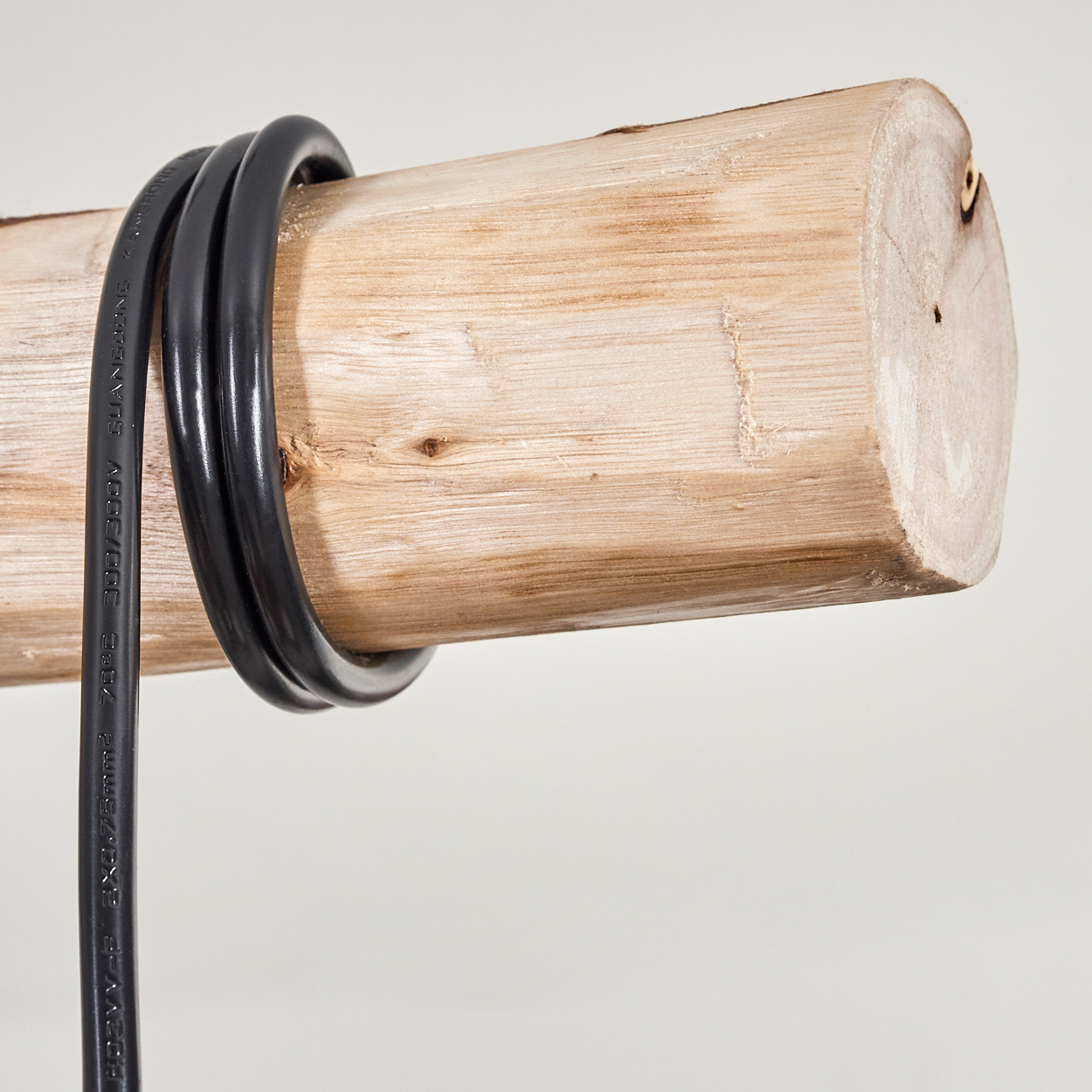 Ein Holzstamm mit einem schwarzen Kabel, das darum gewickelt ist. Der Stamm hat eine hellbraune Farbe. Auf dem Kabel steht Text.