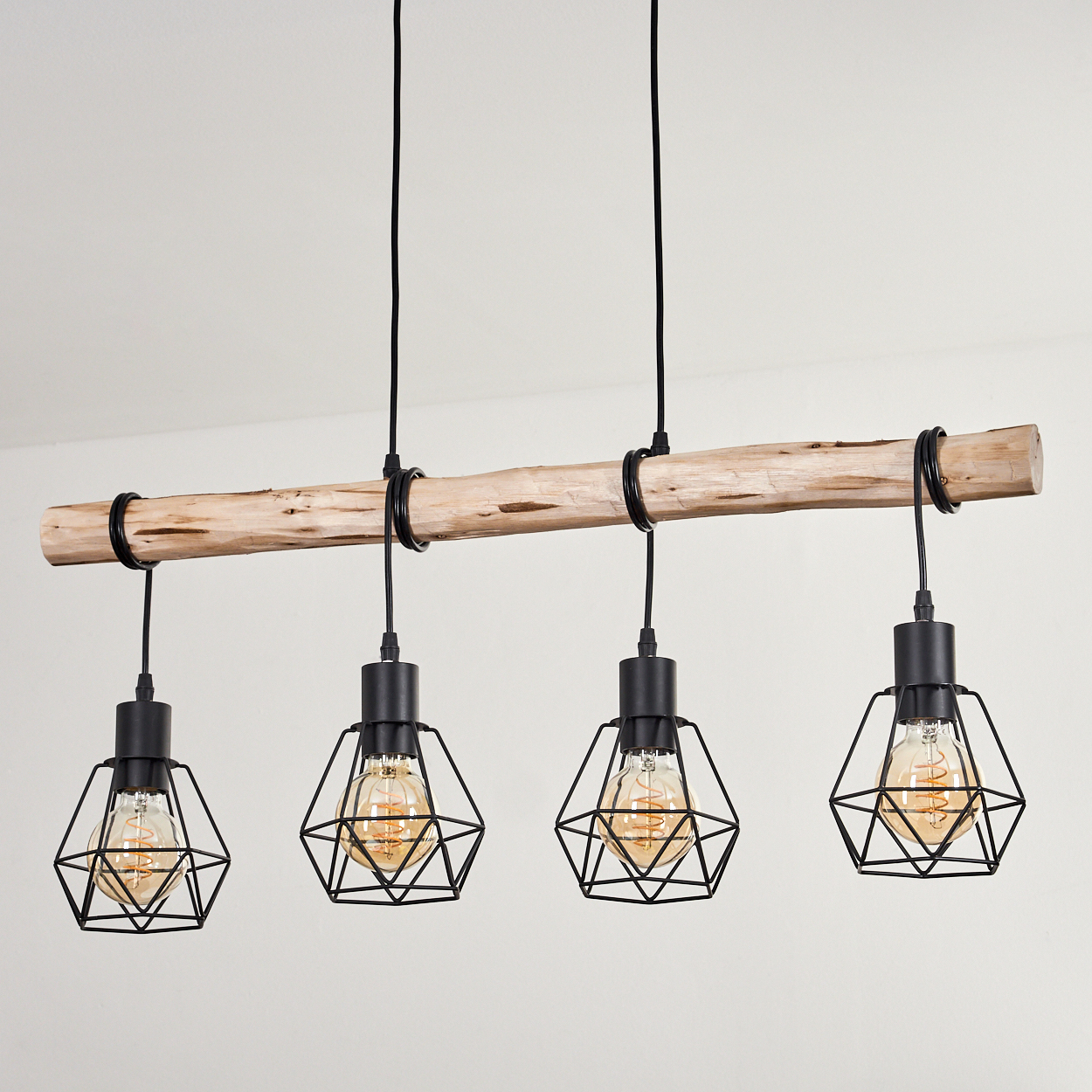 Ein Holzbalken trägt vier schwarze Pendelleuchten mit Edison-Glühbirnen. Der Hintergrund ist eine weiße Wand.