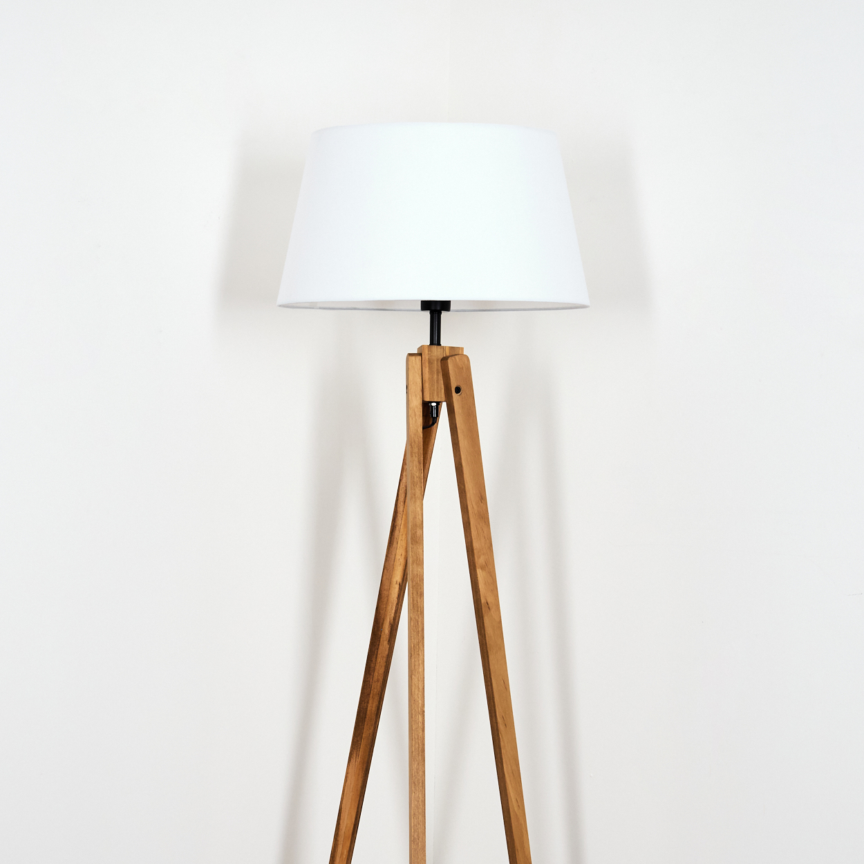Eine Stehlampe aus Holz mit weißem Lampenschirm steht vor einer schlichten weißen Wand. Die Lampe hat ein klassisches Design.