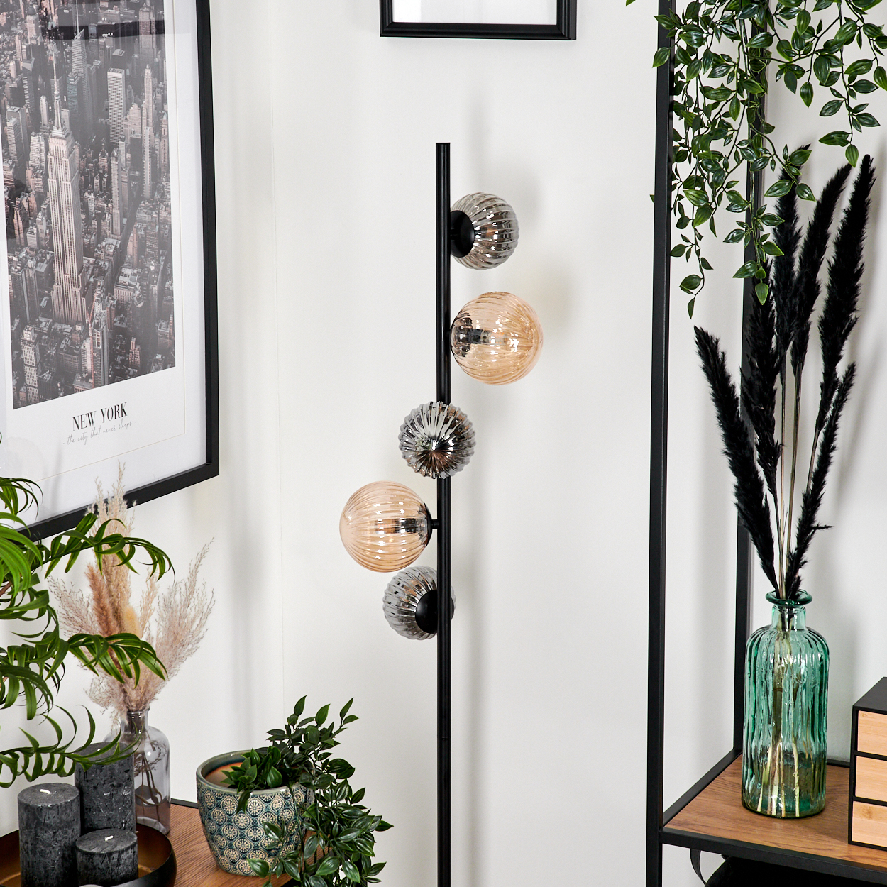 Ein modernes Zimmer mit Stehlampe, Zierpflanzen und einem New York-Bilderrahmen. Die Lampe hat Glaskugeln.
