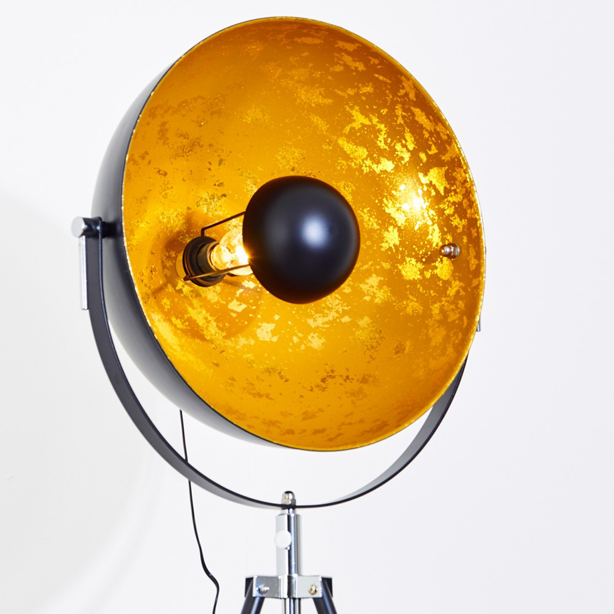 Eine schwarz-goldene Stehlampe. Die Lampe hat ein goldenes Innenleben, ein schwarzes Äußeres und eine schwarze kugelförmige Glühbirne. Sie steht auf einem Stativfuß.