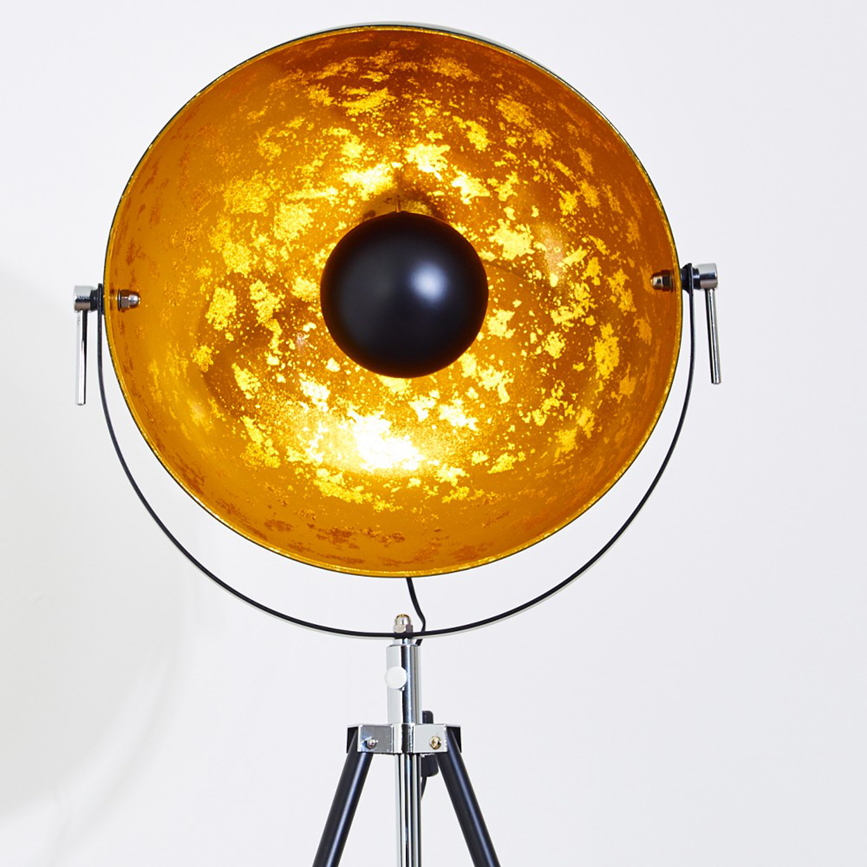Eine große, goldfarbene Lampe mit einer schwarzen Kugel in der Mitte, die von einem schwarzen Stativfuß getragen wird.