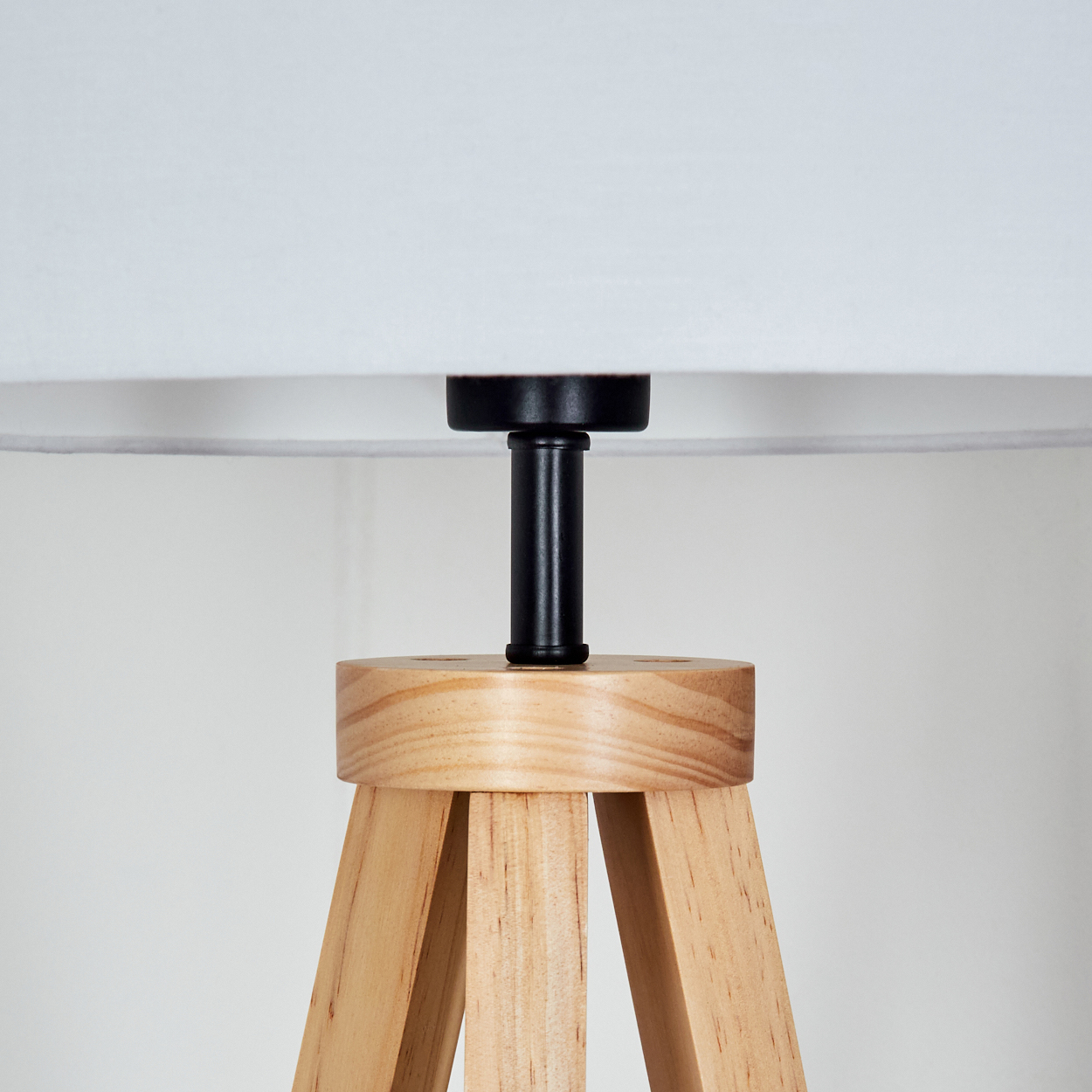 Nahaufnahme einer Lampe. Die Lampe hat einen weißen Lampenschirm, einen schwarzen Stiel und einen Holzfuß, der einem Stativ ähnelt.