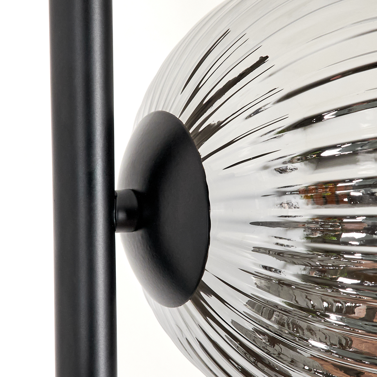 Nahaufnahme einer Lampe. Eine schwarze Metallstange trägt eine gerippte Glaskugel. Die Kugel ist durch ein schwarzes Kreisteil befestigt.