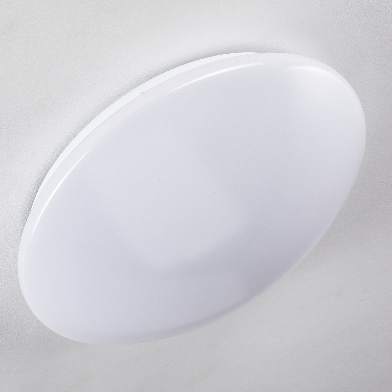 Eine weiße, ovale Deckenleuchte. Sie ist an einer weißen Decke befestigt. Das Licht hat eine glatte, glänzende Oberfläche.