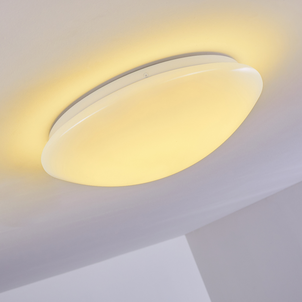 Eine weiße, ovale Deckenleuchte ist zentriert und erzeugt einen warmen Schein. Weiße Decke und Wände umgeben das Licht.