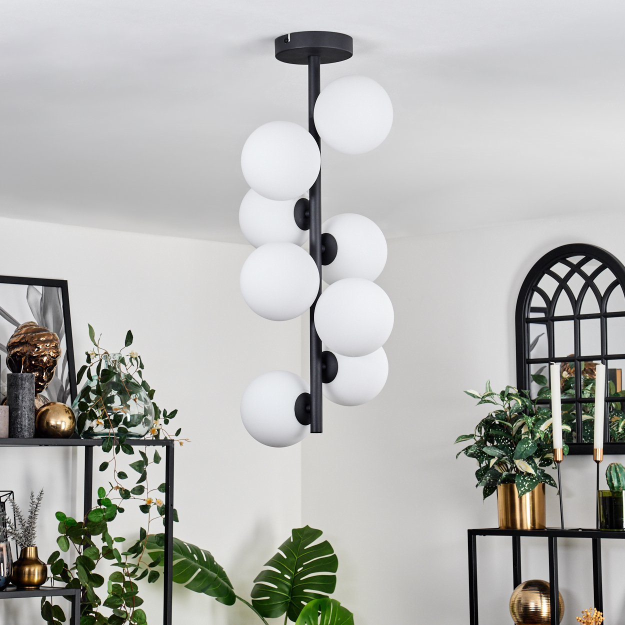 Eine moderne Hängelampe mit weißen Kugeln. Schwarze Regale beherbergen Pflanzen, Dekoration und einen Spiegel. Stilvolles, helles Interieur.