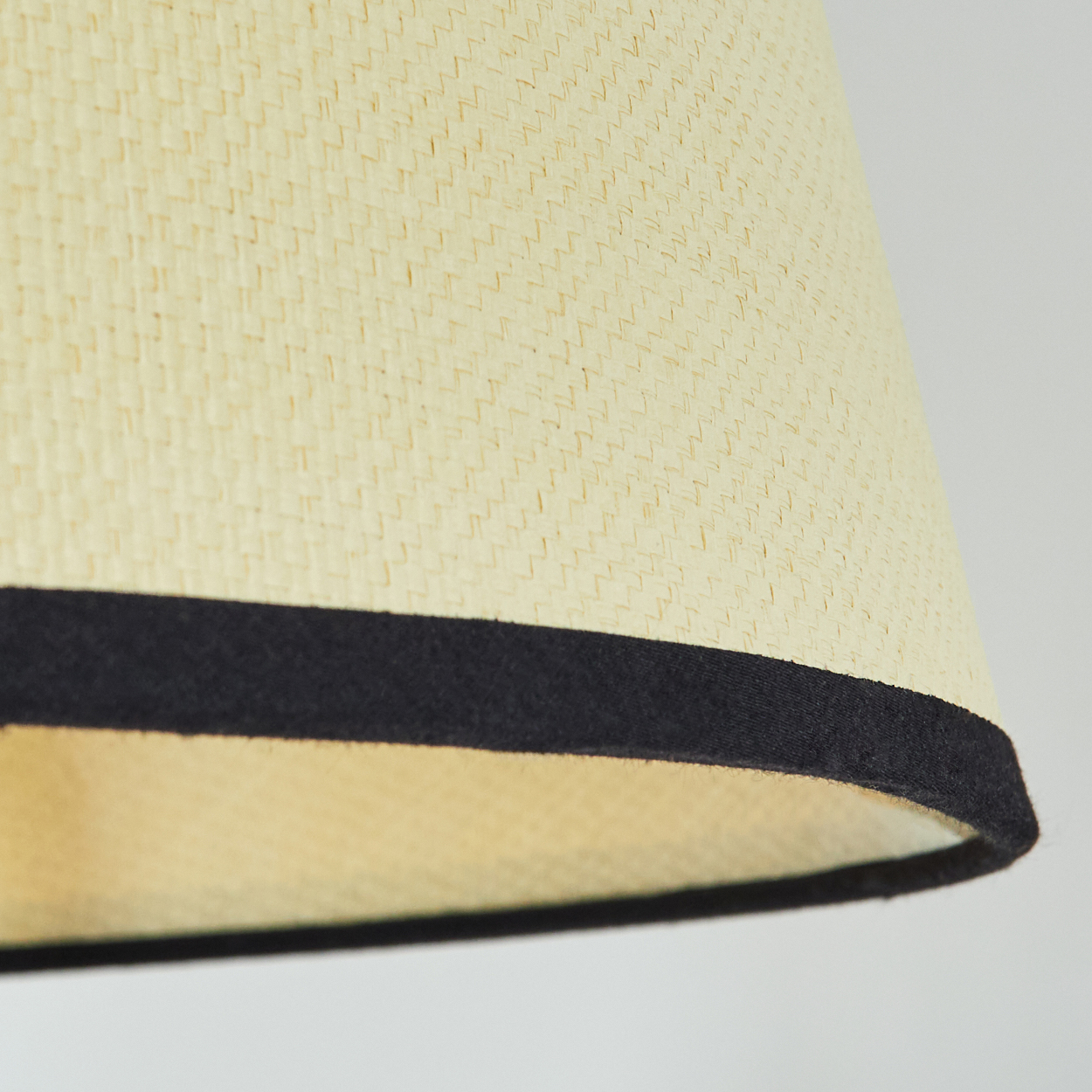 Nahaufnahme eines Lampenschirms. Er ist beige mit schwarzem Besatz am unteren Rand. Der Hintergrund ist einfarbig hell.
