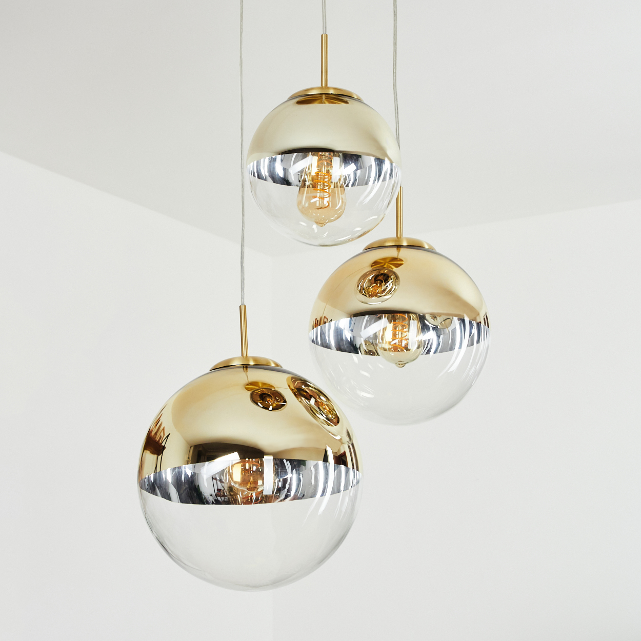 Drei gold- und klarglasfarbene Pendelleuchten hängen von der Decke. Jede hat eine Glühbirne im Inneren.