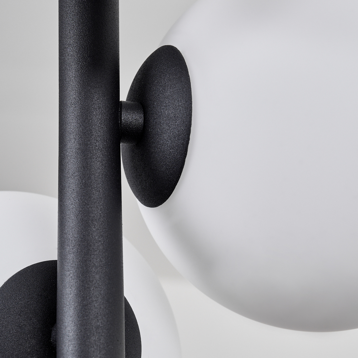 Nahaufnahme einer modernen Lampe. Schwarze Metallstange und runde Halterungen tragen weiße, kugelförmige Glasschirme vor weißem Hintergrund.