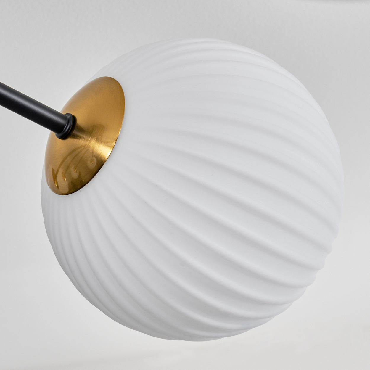 Ein weißer, kugelförmiger Lampenschirm mit goldfarbenem Sockel und schwarzem Arm vor weißem Hintergrund.