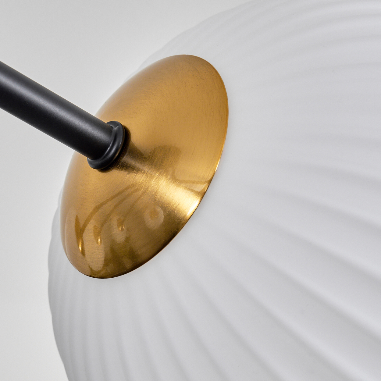 Nahaufnahme eines weißen, gerippten Glaslampenschirms mit goldfarbener Metallkappe und einem schwarzen Arm.