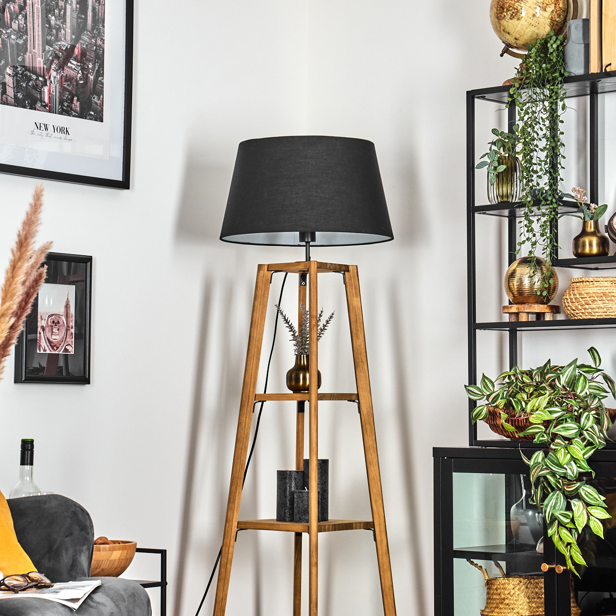 Eine hölzerne Stehlampe mit schwarzem Lampenschirm steht in einem Raum mit einem schwarzen New York-Poster und einem Regal mit Pflanzen.