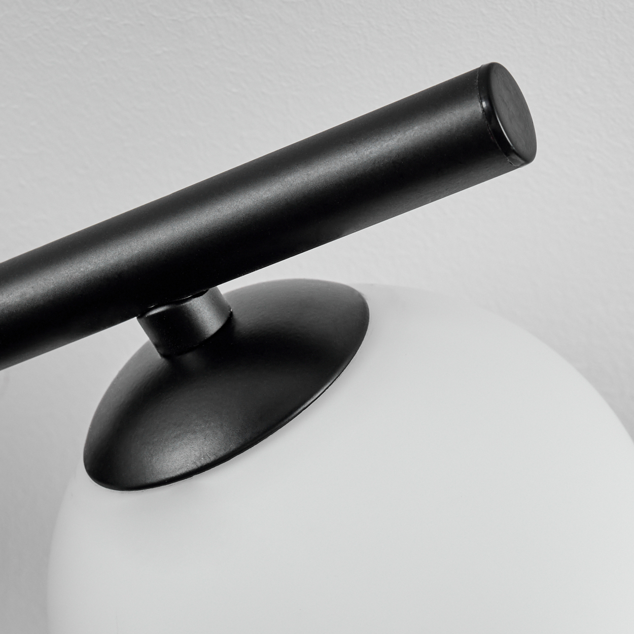 Nahaufnahme eines schwarzen Lampenarms und -fußes auf einer weißen Glaskugel. Der Hintergrund ist eine weiße Wand. Die Lampe hat ein modernes Design.