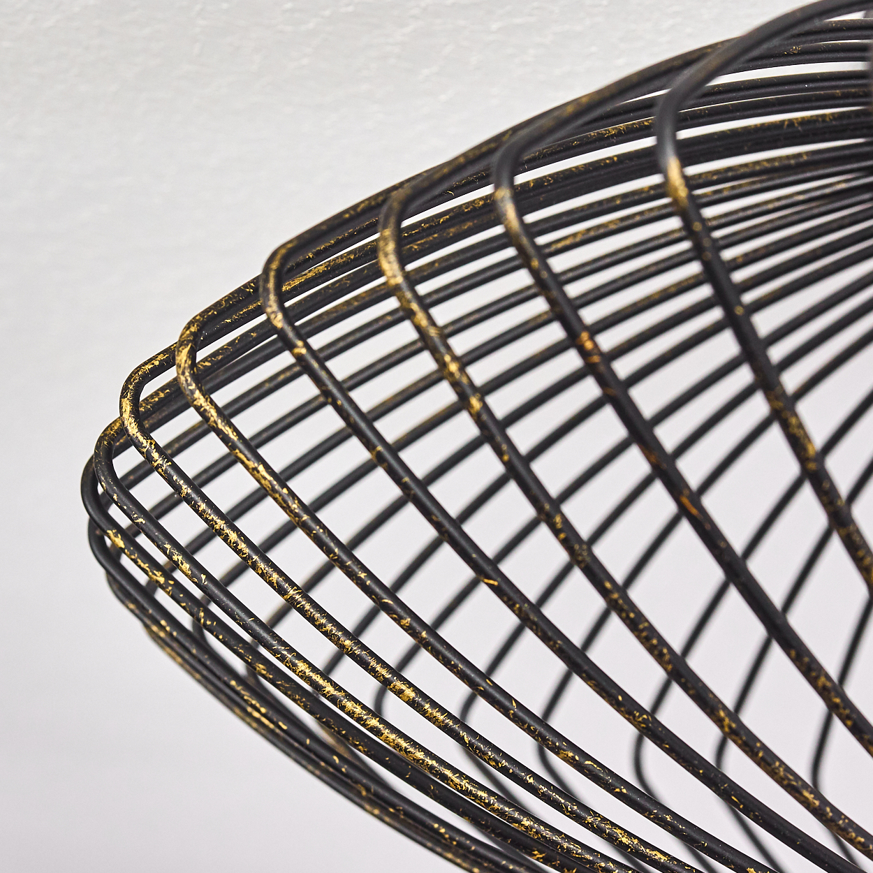 Nahaufnahme eines schwarzen, goldakzentuierten Drahtlampenschirms vor weißem Hintergrund. Der Schirm hat eine konische Form mit Metallstäben.