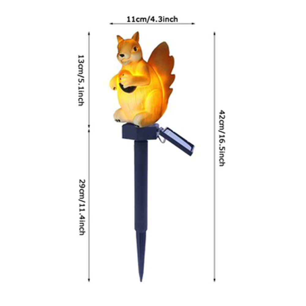 Ein eichhörnchenförmiges Gartenlicht. Es ist ein solarbetriebener Pfahl mit einer Eichhörnchenfigur oben, die eine Nuss hält. Das Licht leuchtet orange.