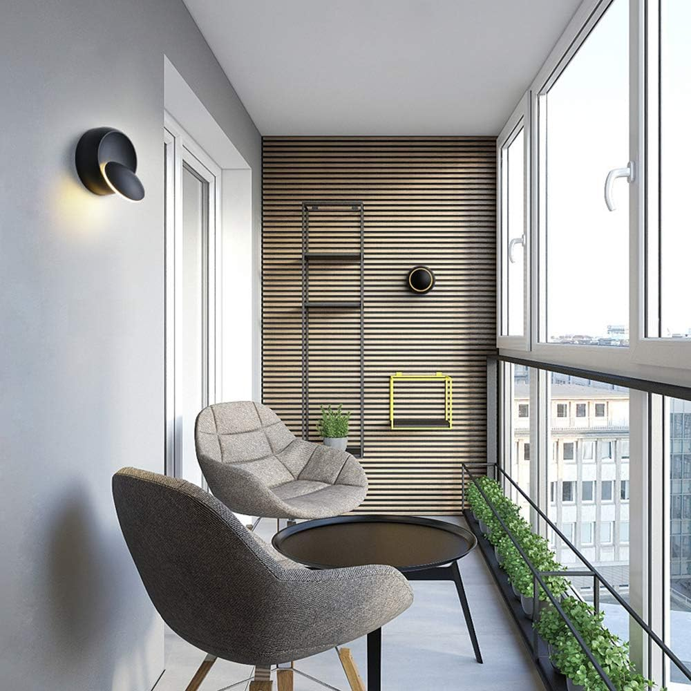 Balkon mit zwei grauen Stühlen, schwarzem Tisch, Holzwand, schwarzen Regalen und einem Fenster mit Blick auf Gebäude.