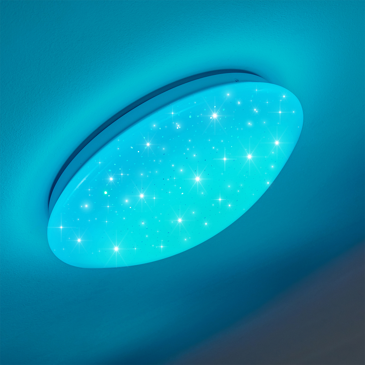 Eine ovale Deckenleuchte mit Sternenmuster. Das Licht strahlt blau, vor blauem Himmel und Wand.