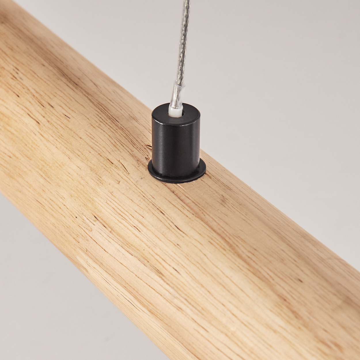 Ein Holzbalken mit einem schwarzen Metallzylinder, an dem ein silbernes Kabel befestigt ist, vor weißem Hintergrund.