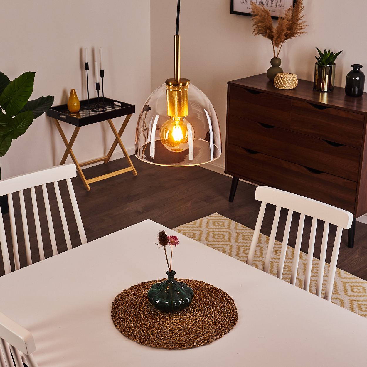 Ein Esszimmer mit einem weißen Tisch, Stühlen und einer Hängeleuchte. Auf dem Tisch steht eine Vase mit Blumen.