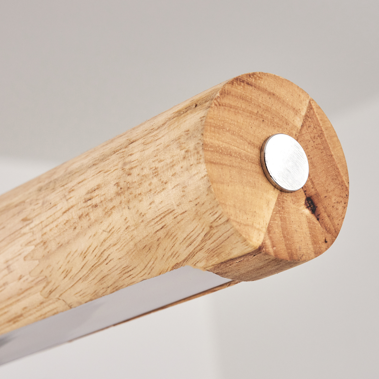 Nahaufnahme eines Holz zylinders mit einer silbernen Scheibe an seinem Ende. Das Holz hat eine natürliche Maserung. Ein Metallstreifen ist unten sichtbar.