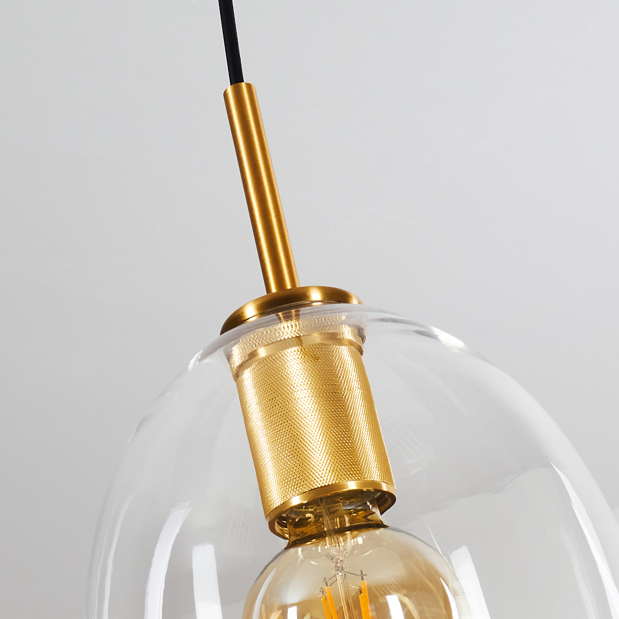 Eine klare Glas-Pendelleuchte mit goldenen Akzenten und einer sichtbaren Glühbirne. Der Hintergrund ist schlicht weiß.