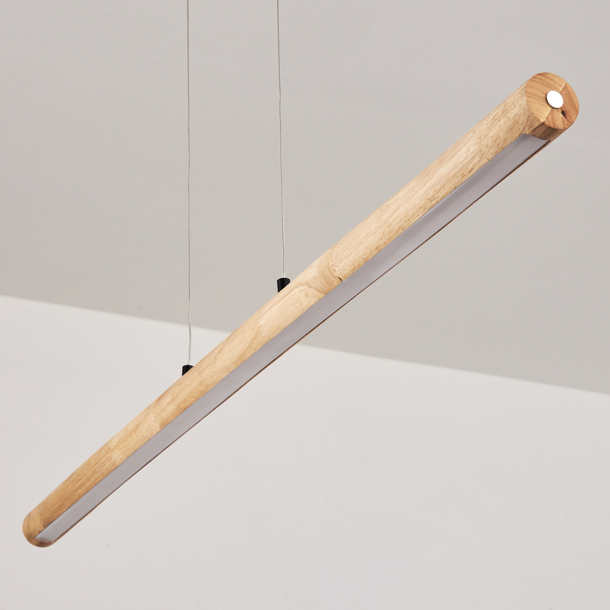 Eine zylindrische Holzleuchte hängt von der Decke. Sie hat einen hellen, rechteckigen Lichtstreifen entlang der Unterkante.