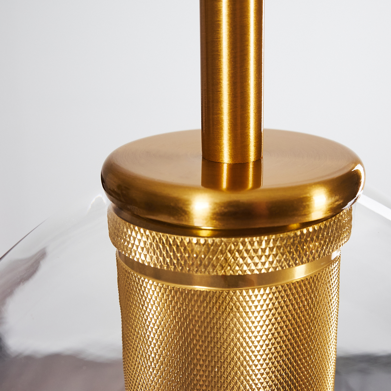 Nahaufnahme eines goldenen Lampenfußes. Er hat einen strukturierten Boden, eine glatte Oberseite und eine goldene Mittelstange. Der Hintergrund ist weiß und reflektierend.