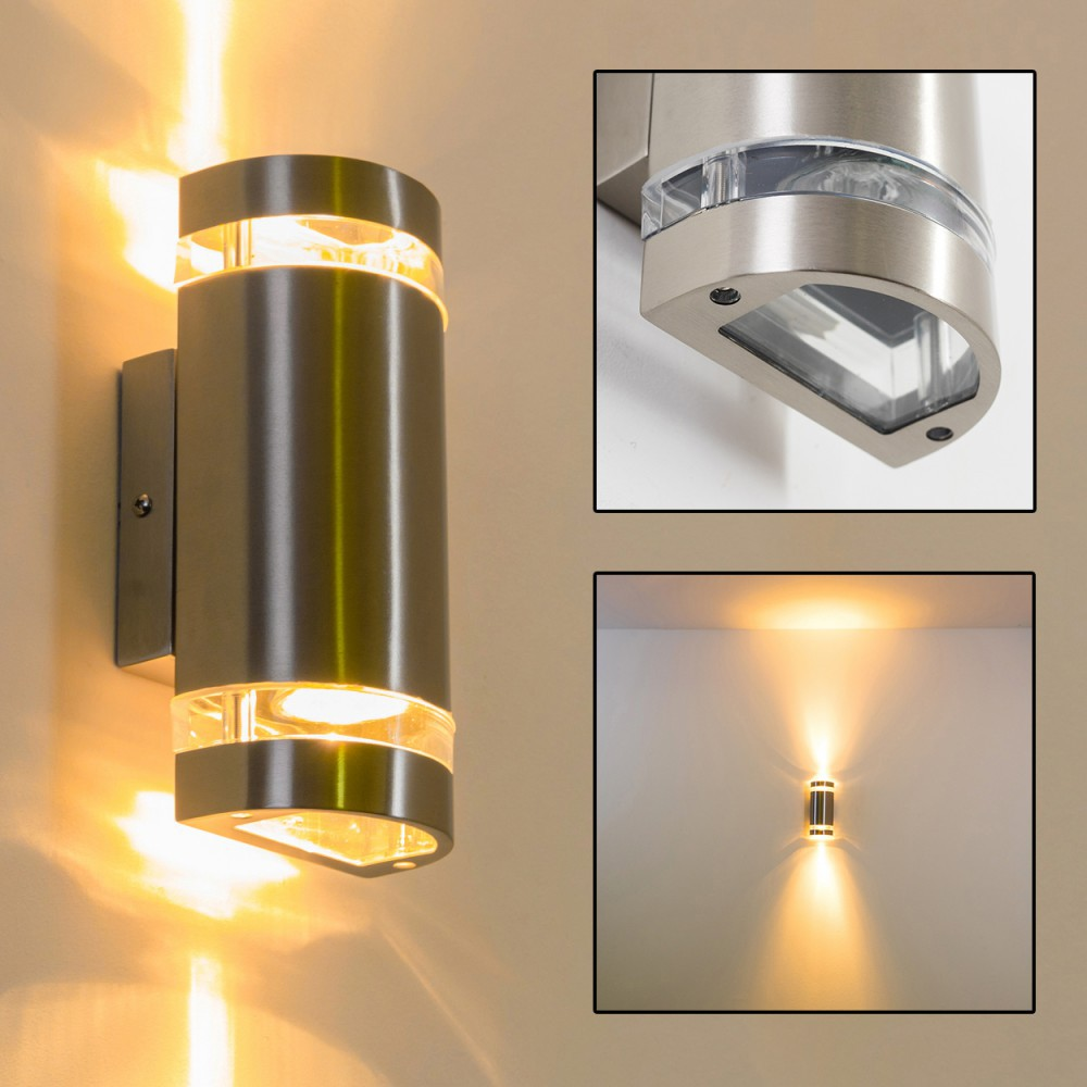 Eine silberne Wandleuchte ist an einer hellen Wand montiert. Die Lampe hat ein oberes und unteres Licht. Nahaufnahmen sind vorhanden.