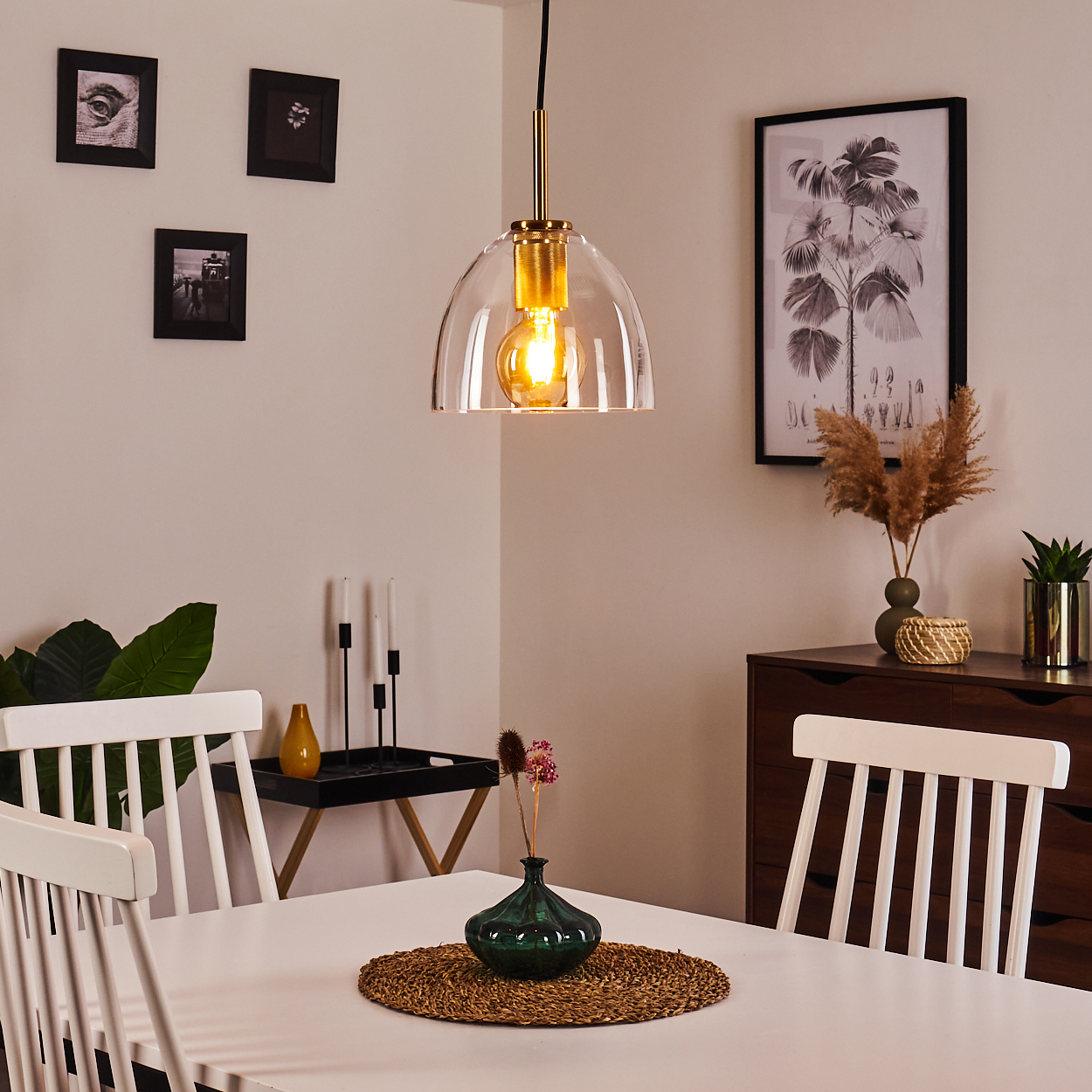 Ein Esszimmer mit weißem Tisch, Stühlen und Hängelampe. Dekorationen umfassen eine Vase mit Blumen und gerahmte Kunstwerke.