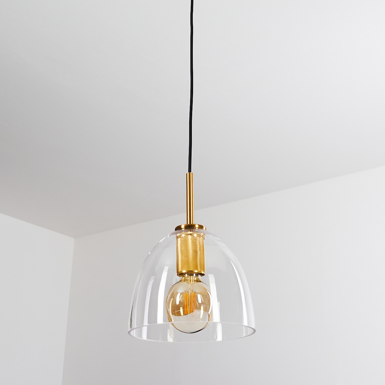 Eine moderne Pendelleuchte hängt von der Decke. Sie hat eine klare Kuppel, eine goldene Fassung und eine sichtbare Glühbirne.