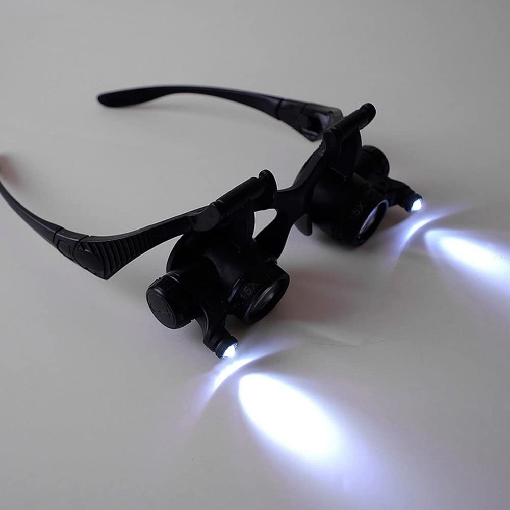 Schwarze Lupenbrille mit LED-Leuchten liegt auf weißer Oberfläche. Die Lichter sind an und beleuchten den Bereich vor ihnen.