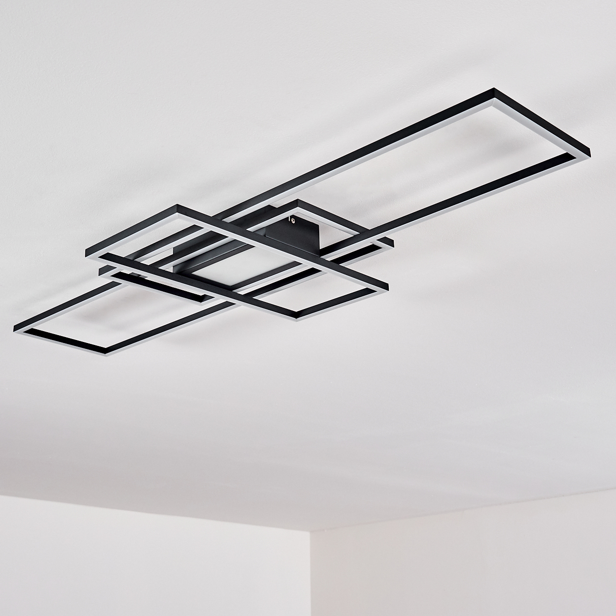 Eine moderne Deckenleuchte mit sich überlappenden schwarzen und silbernen rechteckigen Rahmen ist an einer weißen Decke montiert.