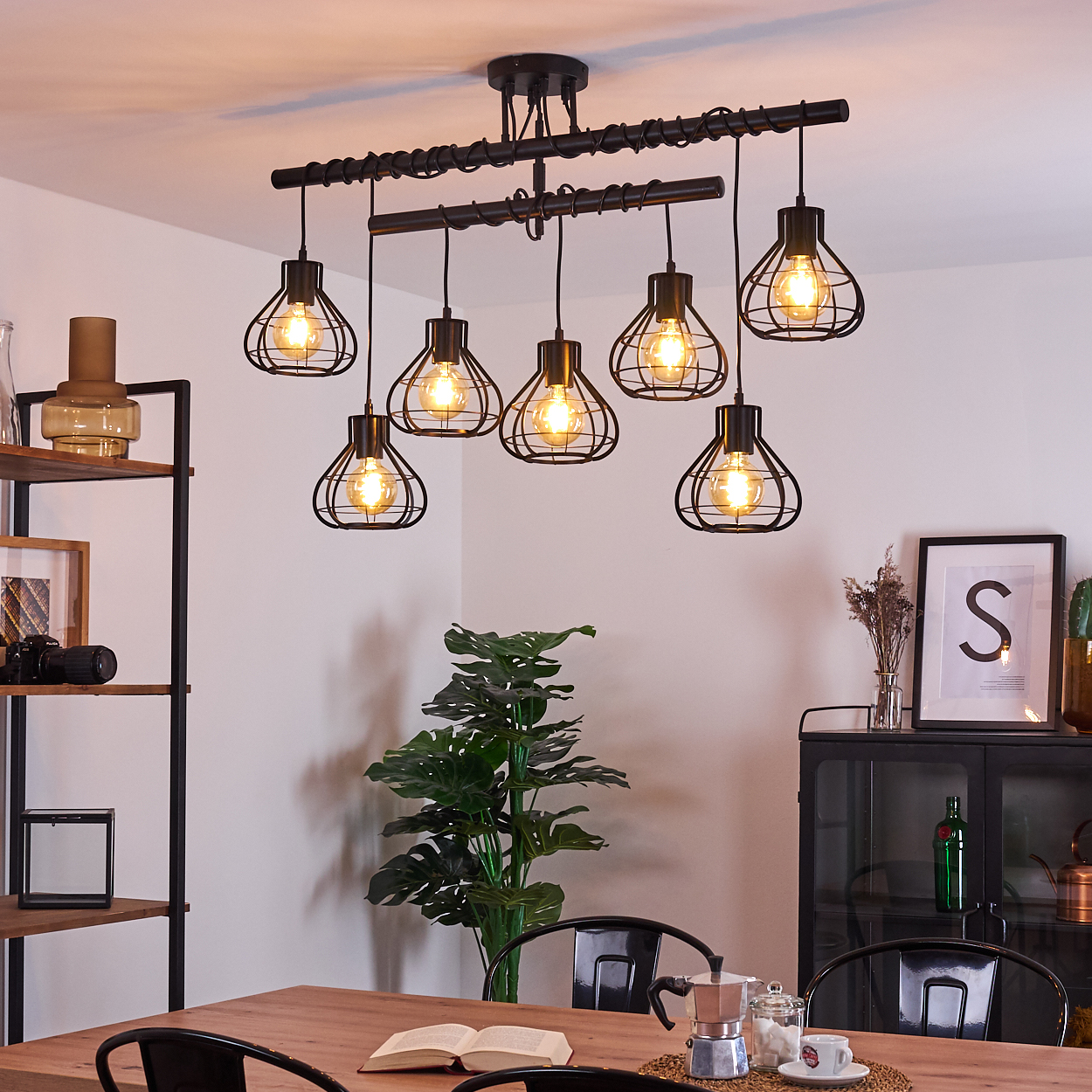 Esszimmer mit Holztisch, schwarzen Stühlen, Hängeleuchte und großer grüner Pflanze.