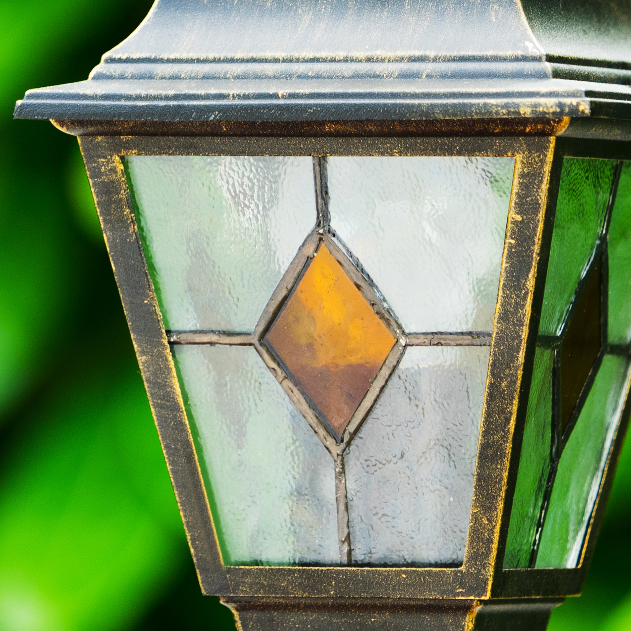 Nahaufnahme einer dekorativen Außenlampe mit Buntglasdesign. Die Lampe hat einen rautenförmigen, bernsteinfarbenen Mittelpunkt.