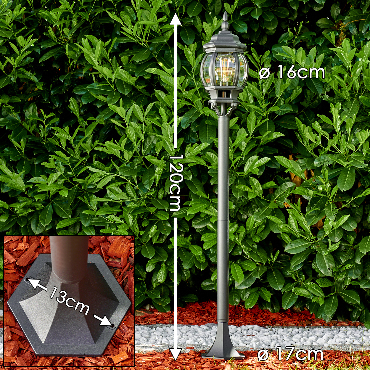 Eine graue Straßenlaterne steht vor grünen Blättern. Die Basis befindet sich auf roter Mulche. Abmessungen der Lampe sind angegeben.