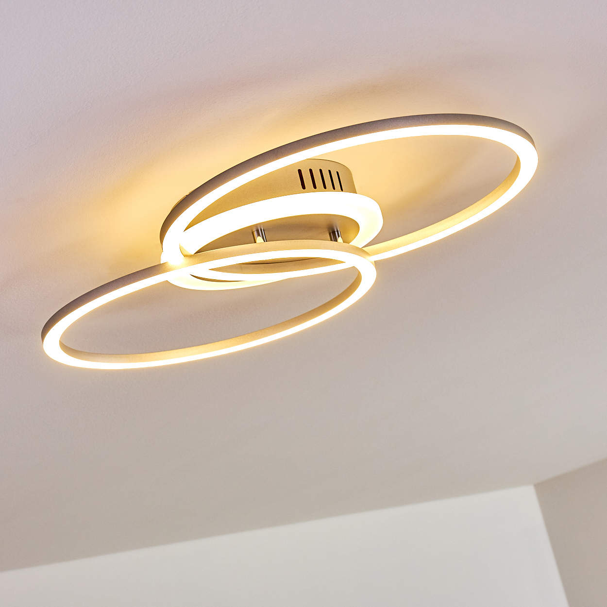 Moderne Deckenleuchte mit drei sich kreuzenden, beleuchteten Ringen. Warmweißes Licht, an einer weißen Decke montiert.
